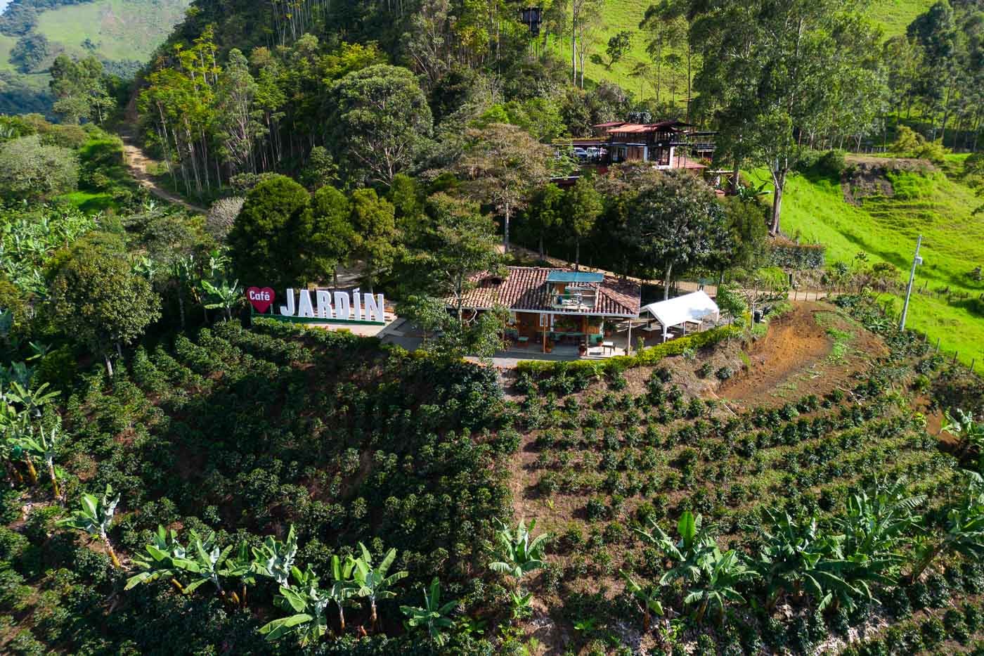 An aerial view of the Café Jardín building and sign on the top of a hill surrounded by trees and bushes.