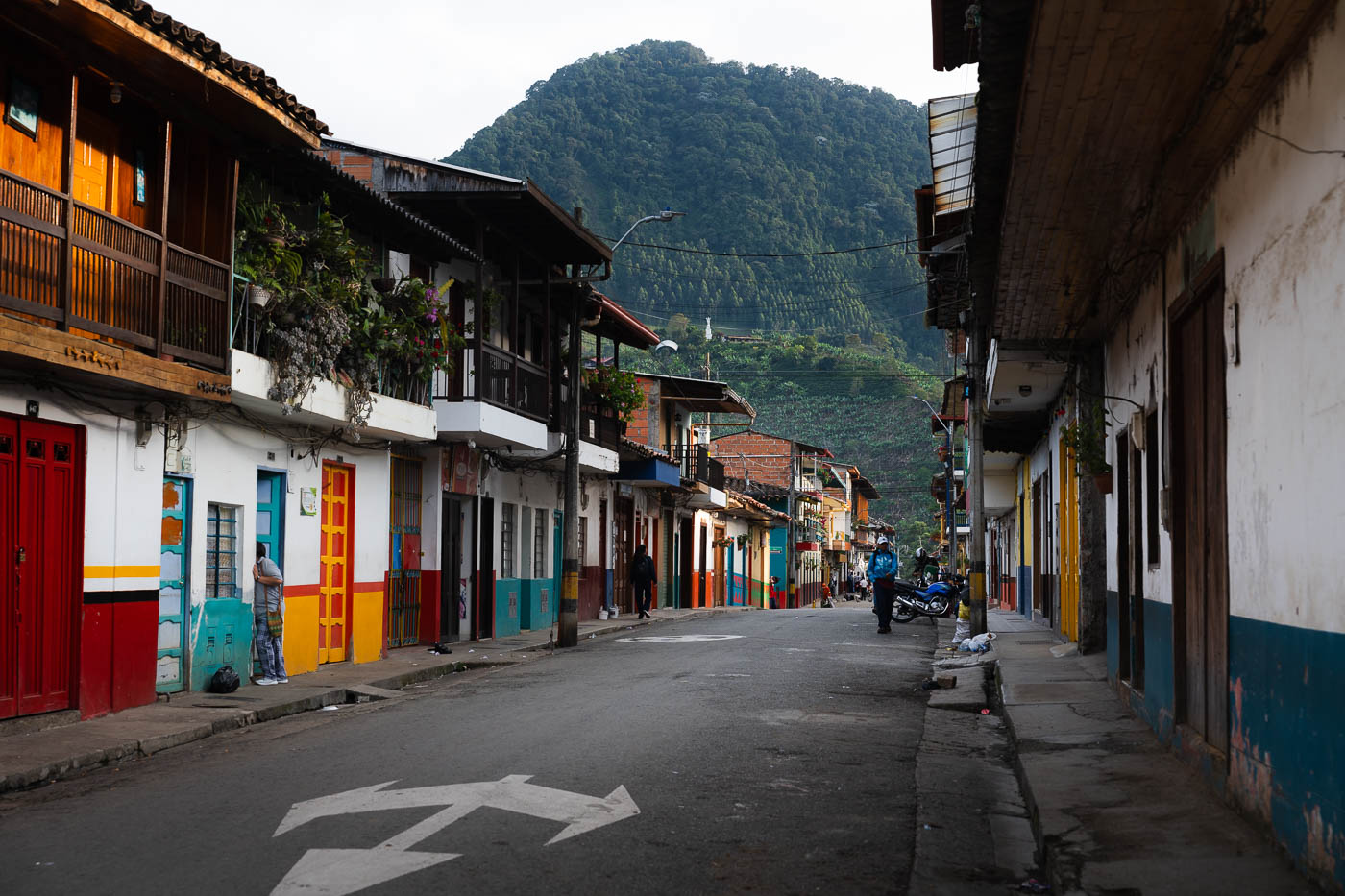 An empty but colourful Jardin street while locals go about their day with mountains in the distance.