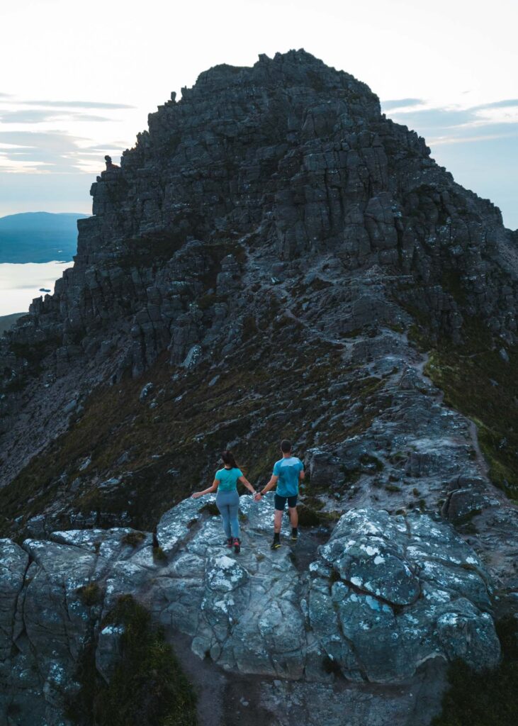 Ryan and Sara holding hands standing at the summit of Stac Pollaidh, a mountain in Scotland.