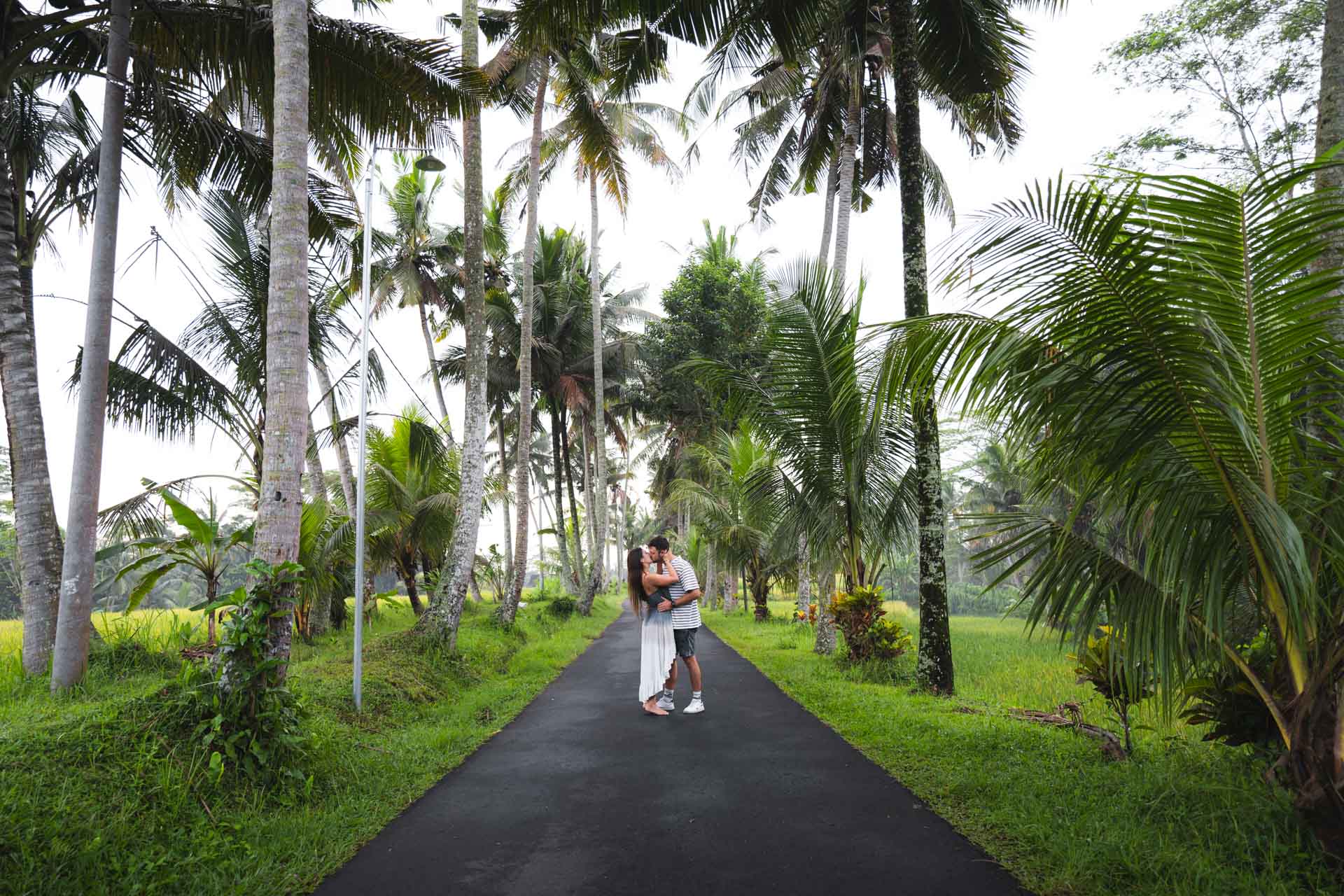 Sara and Ryan kissing on a road lined with palm trees in Bali.