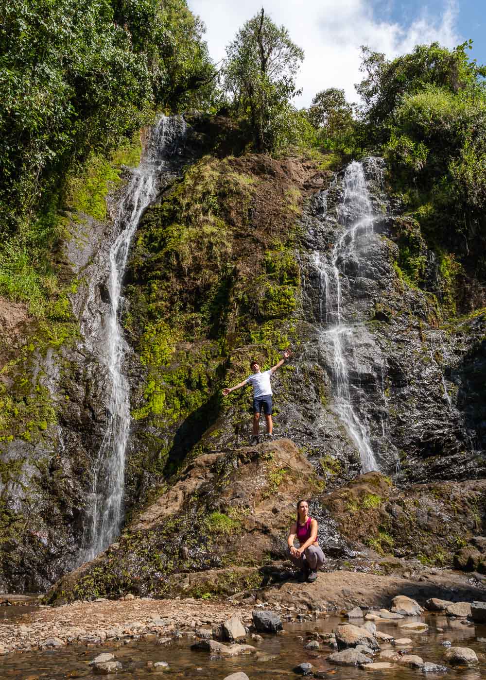 Ryan standing on a rock on the middle Cascada la Escalera while Sara squats in front of it.