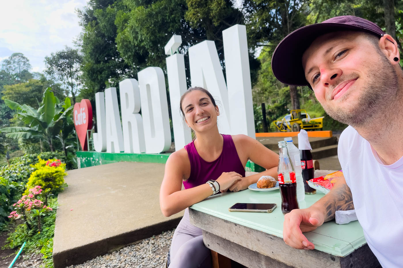 A selfie of Ryan and Sara next to the giant Cafe Jardin sign with some cokes and a cinnamon roll.