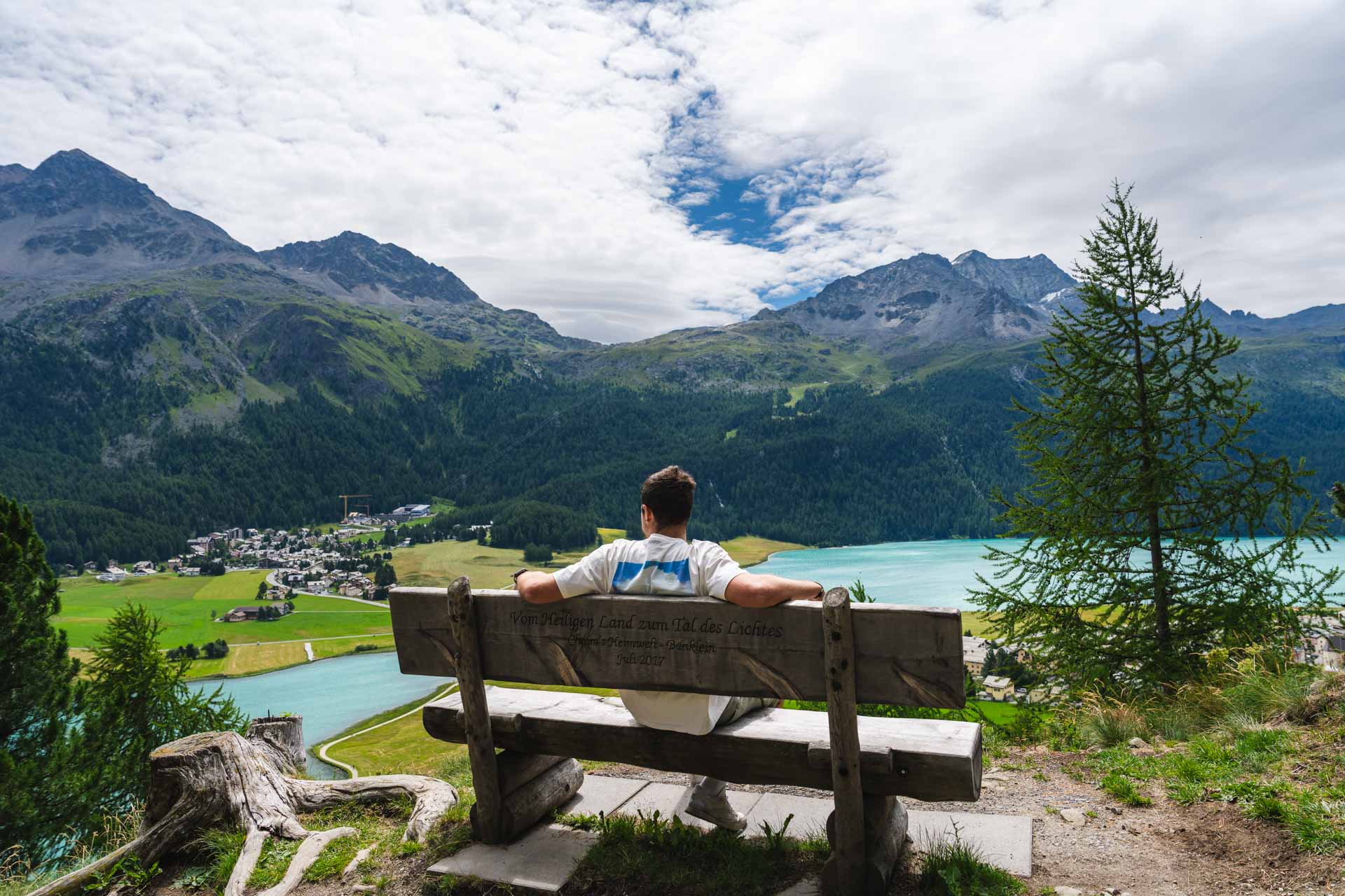 Ryan sitting on a wooden bench in the Swiss mountains overlooking the baby-blue Silverplana Lake.