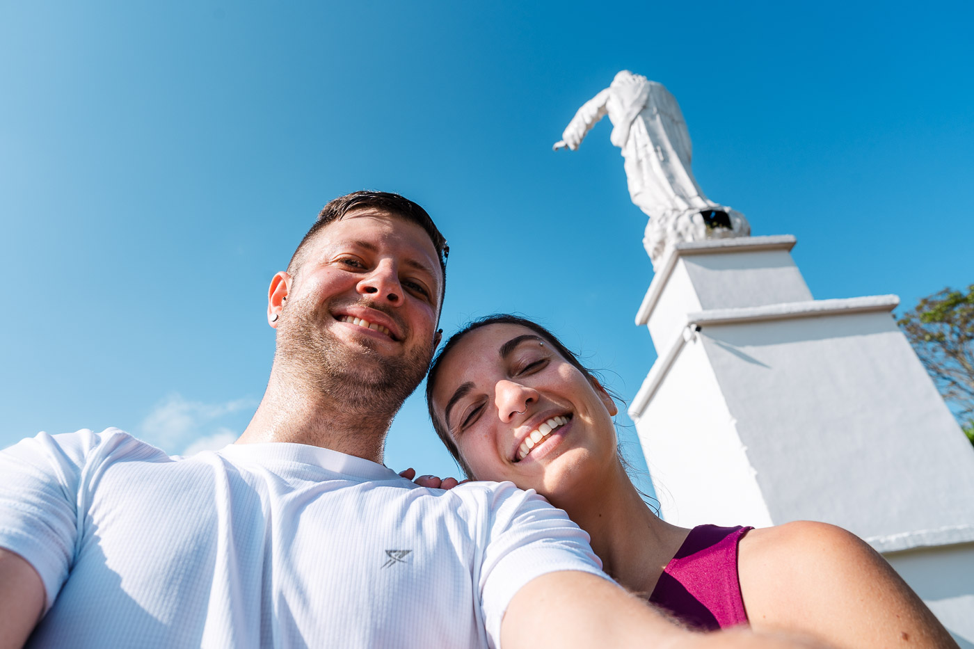 A selfie of Ryan and Sara standing under the Cristo Rey statue on a sunny day.