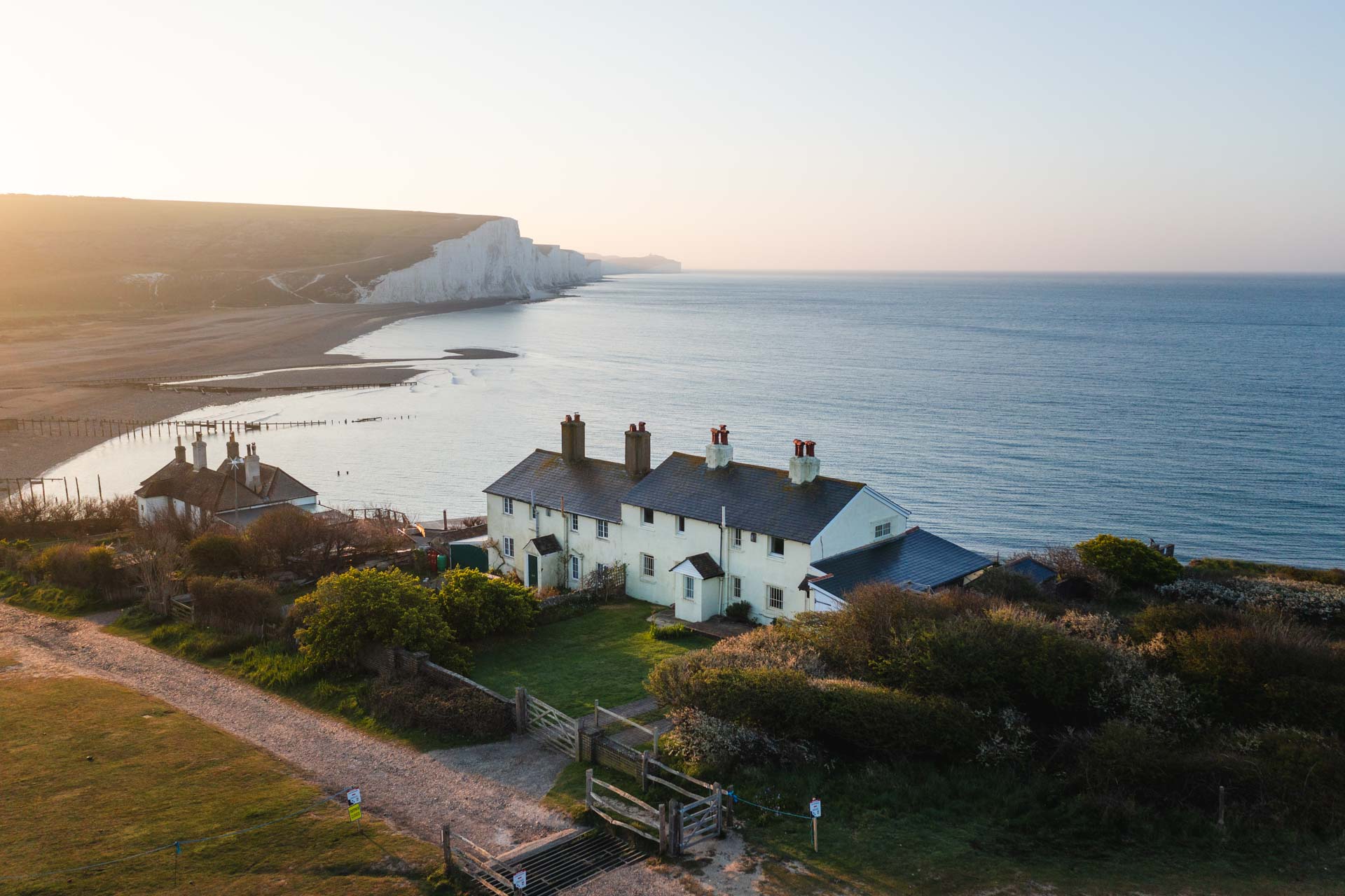 Sunrise light glowing over the lifeguard houses at Cuckmere Haven with the Seven Sisters Cliffs in the background.