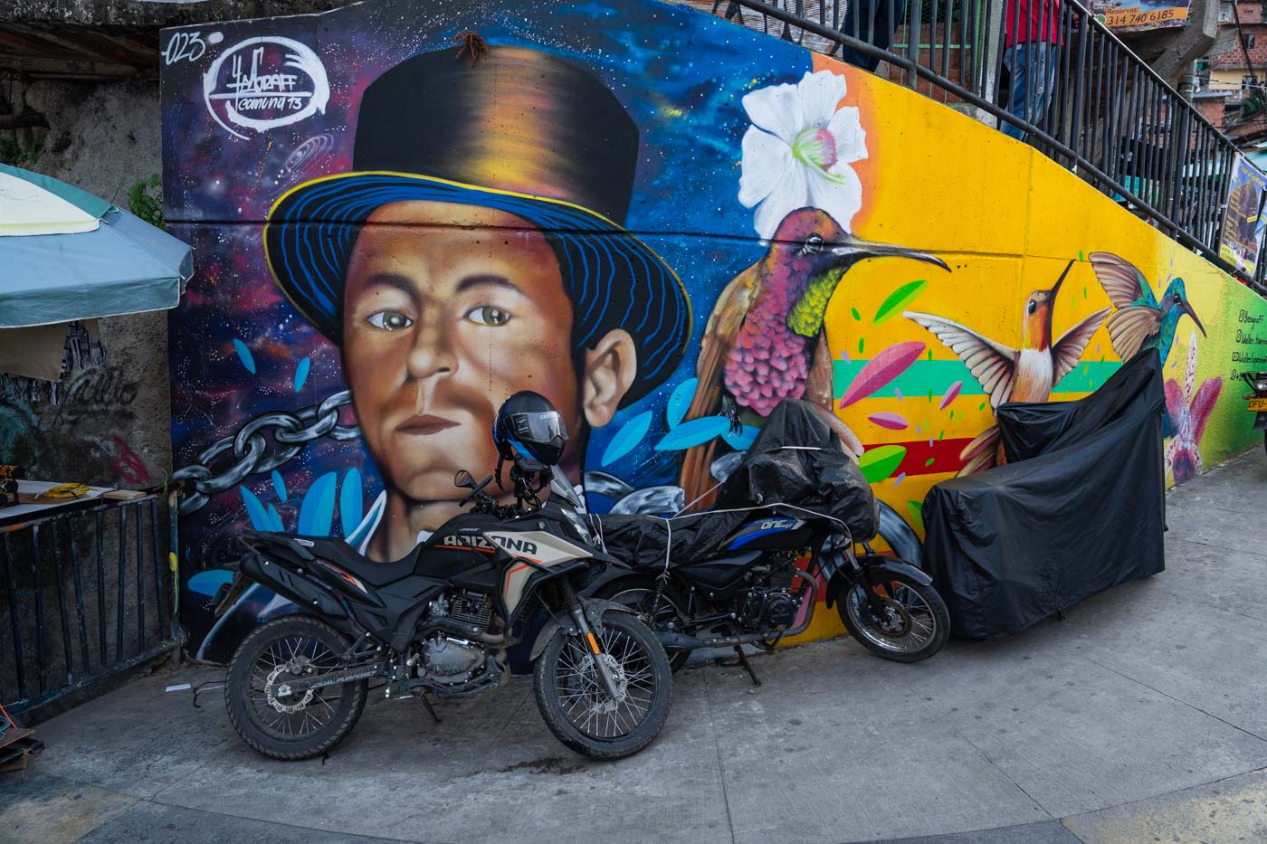 Three bikes parked besides street art depicting a man in a top hat and hummingbirds.