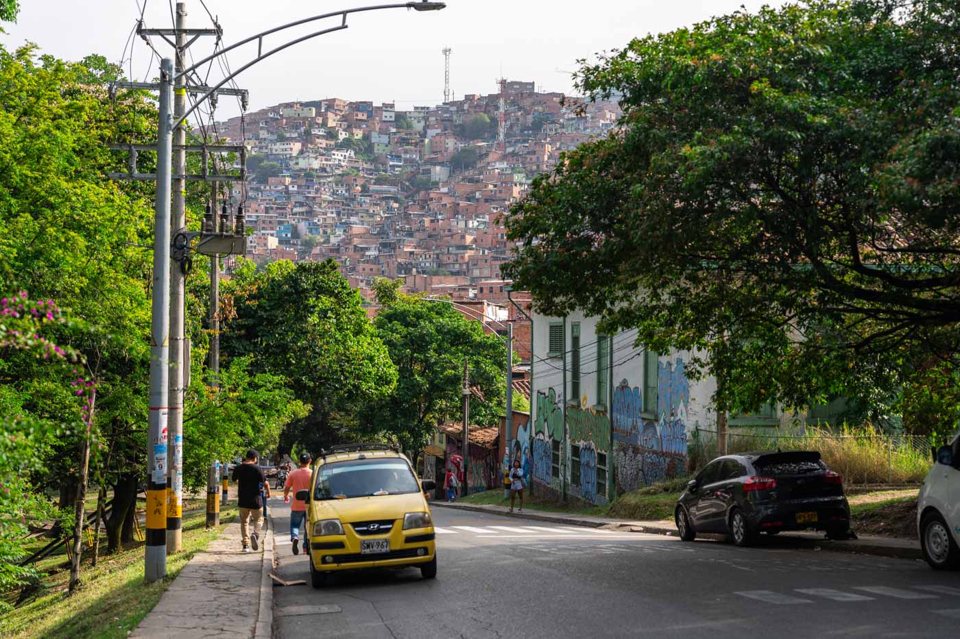 A tree-lined street with a view of the Comuna 13 favelas in the distance.