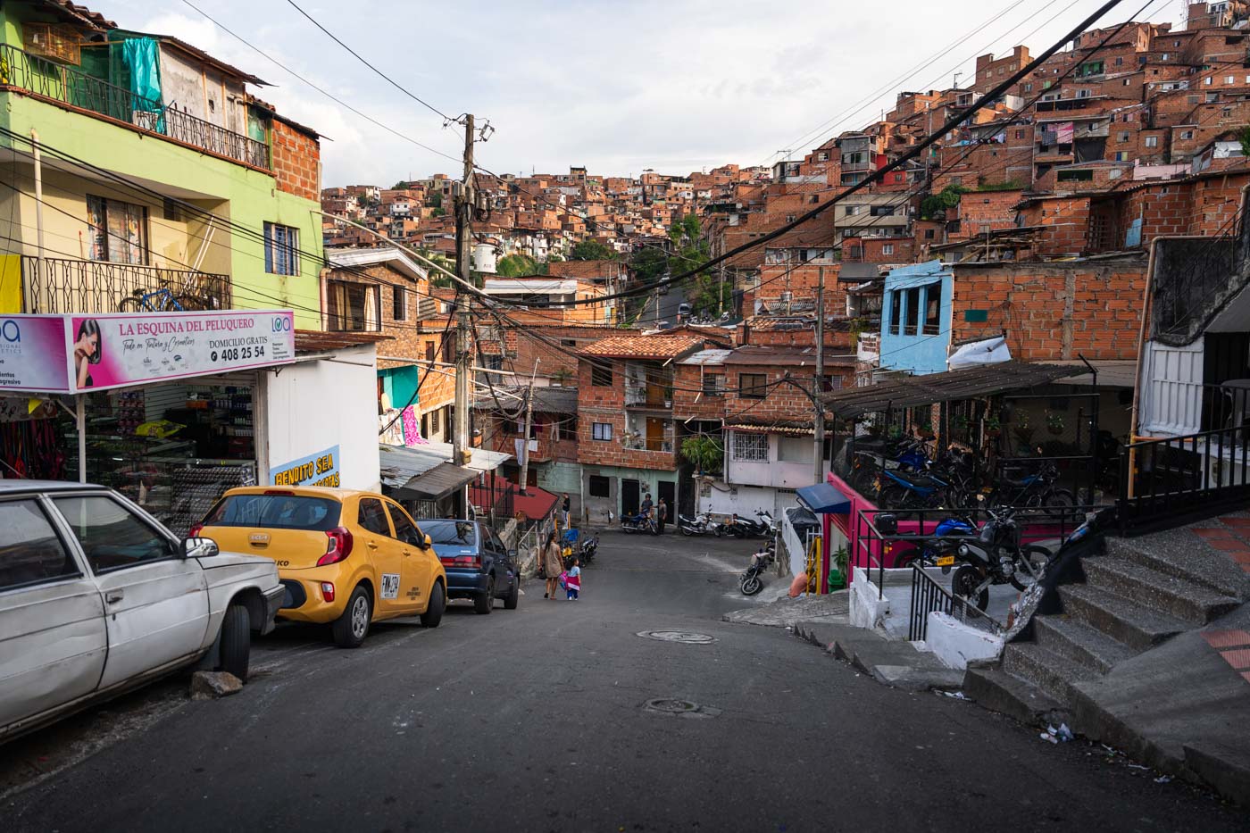 A mother walking her child on a ground level street with favelas behind.