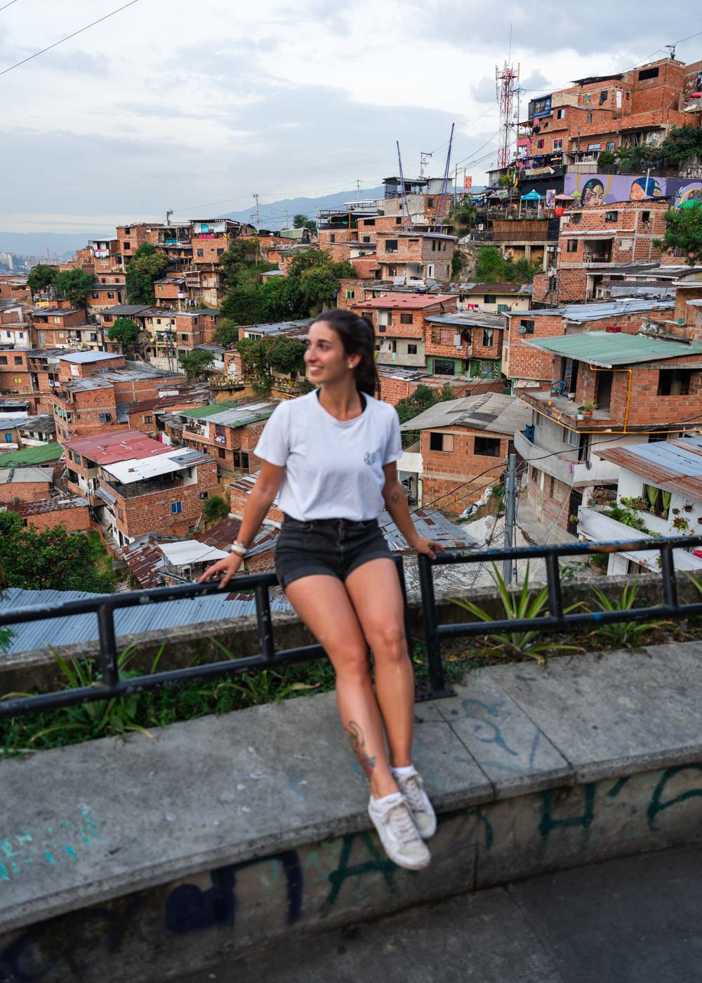 Sara sitting on a railing with a backdrop of the brick houses built on the hill of Comuna 13.