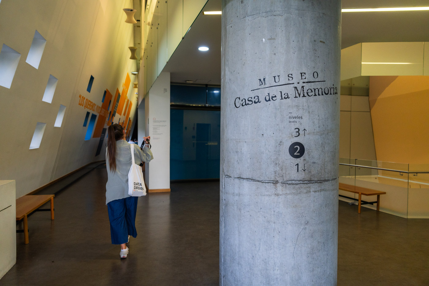 Sara walking past a cement column at the entrance of the Casa de la Memoria museum in Medellin.