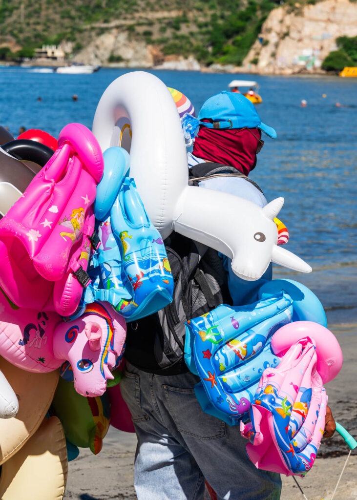 A seller walking up the beach holding inflatables.