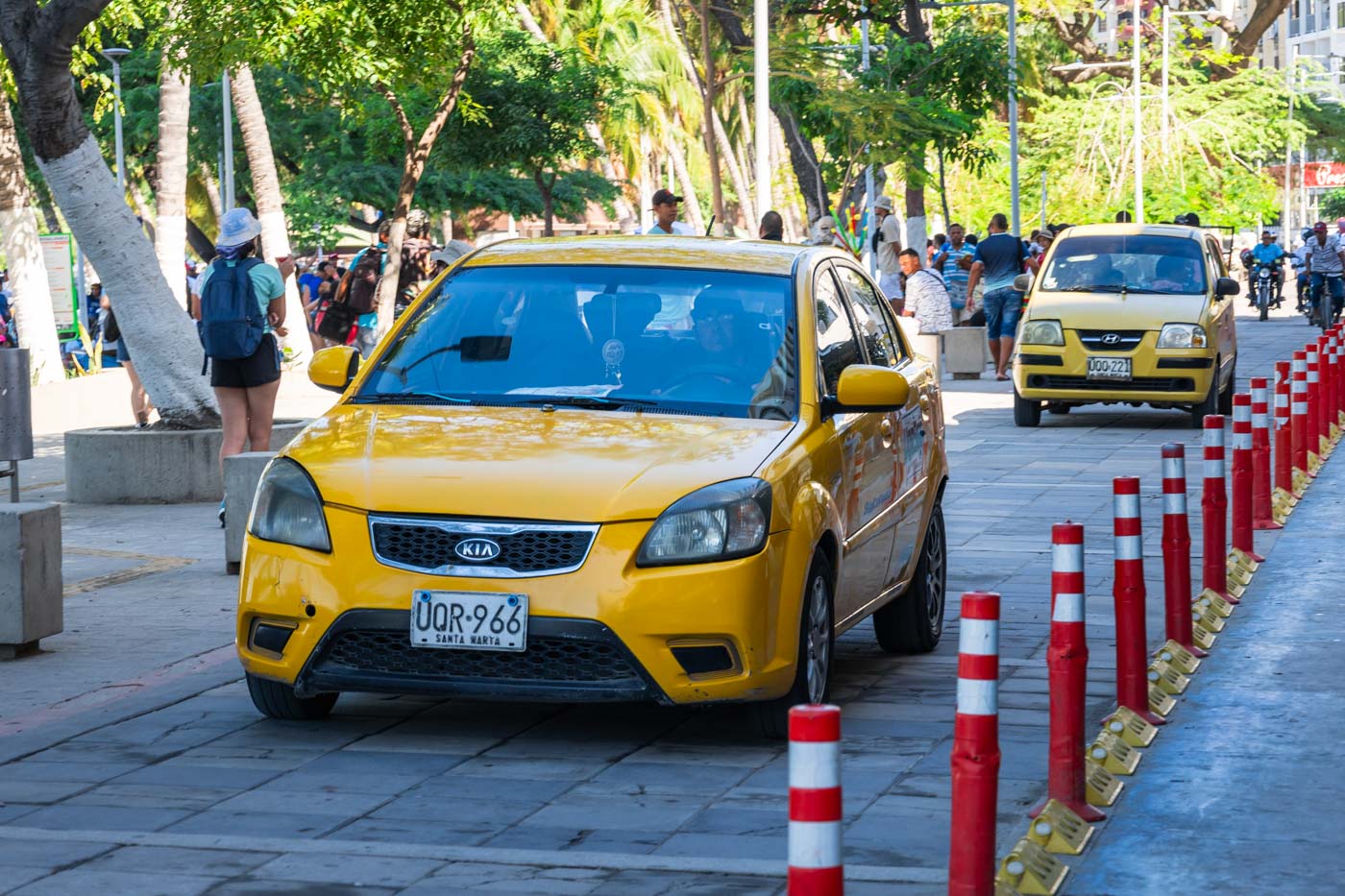 Two yellow taxi's driving along Rodadero promenade past crowds of tourists.