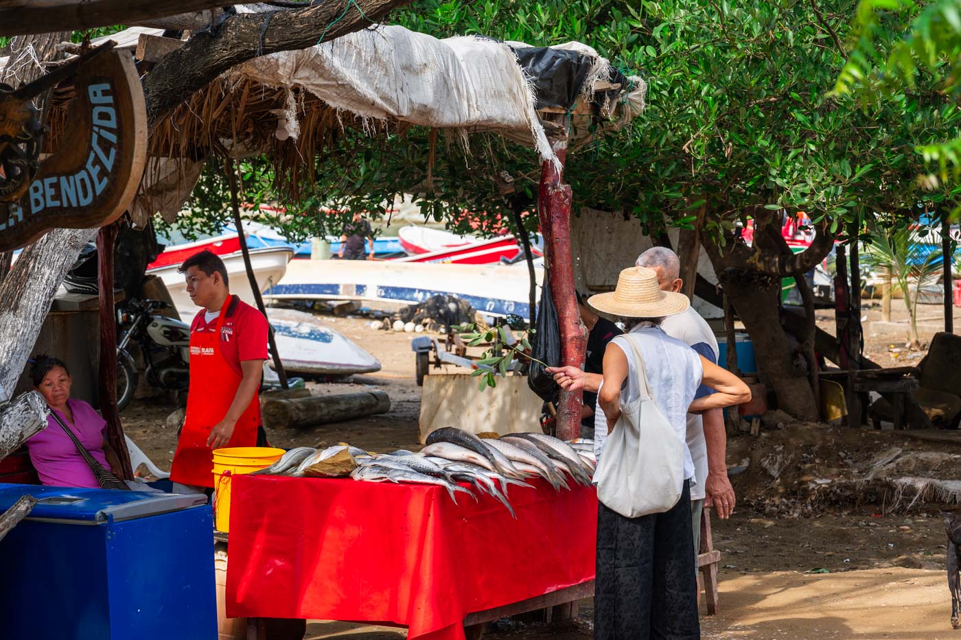 Two people shopping at a fresh fish stall covered in a red cloth in Taganga.