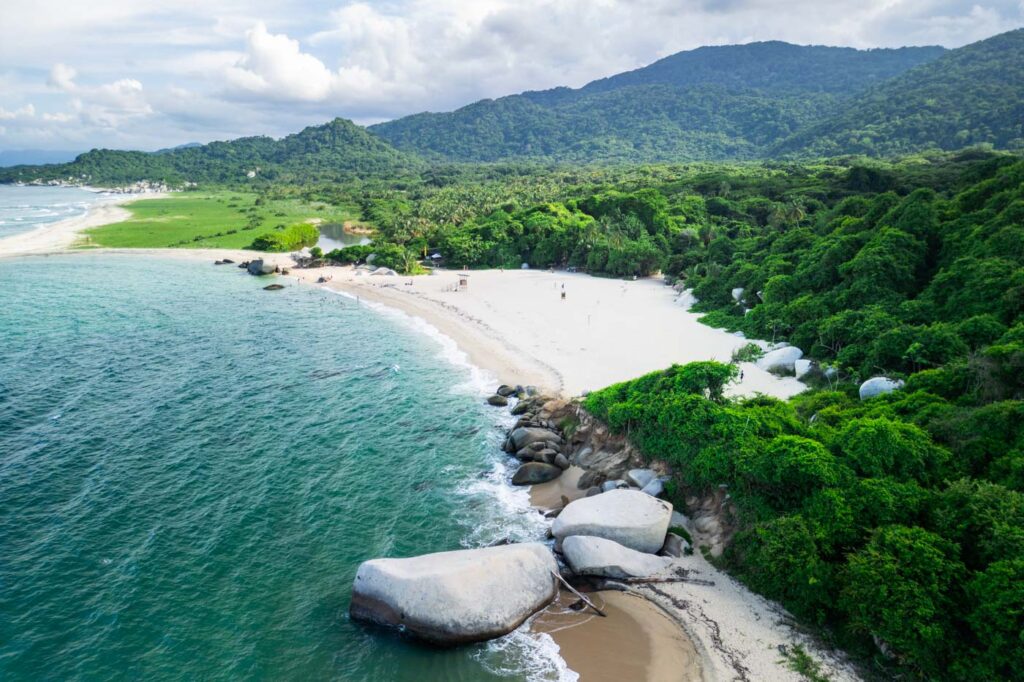 Aerial view over Playa Arenilla surrounded by ocean, rocks and forest in Tayrona beside La Piscina.