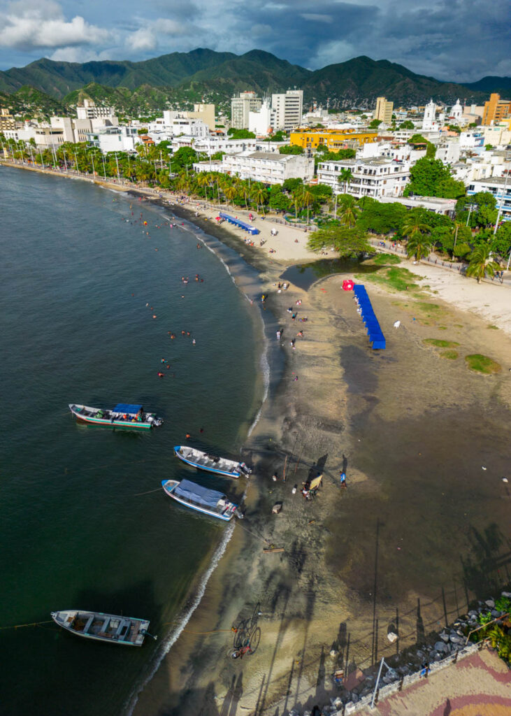 A drone shot of a small and dirty Santa Marta beach with mountains in the distance.