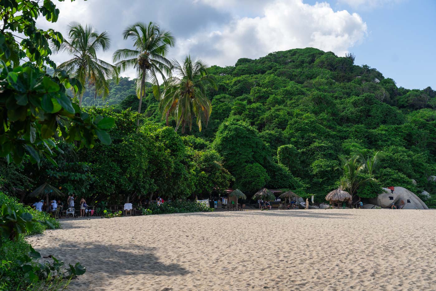 A few tourists and cabanas in the tree line along Playa Arenilla in Tayrona National Park.