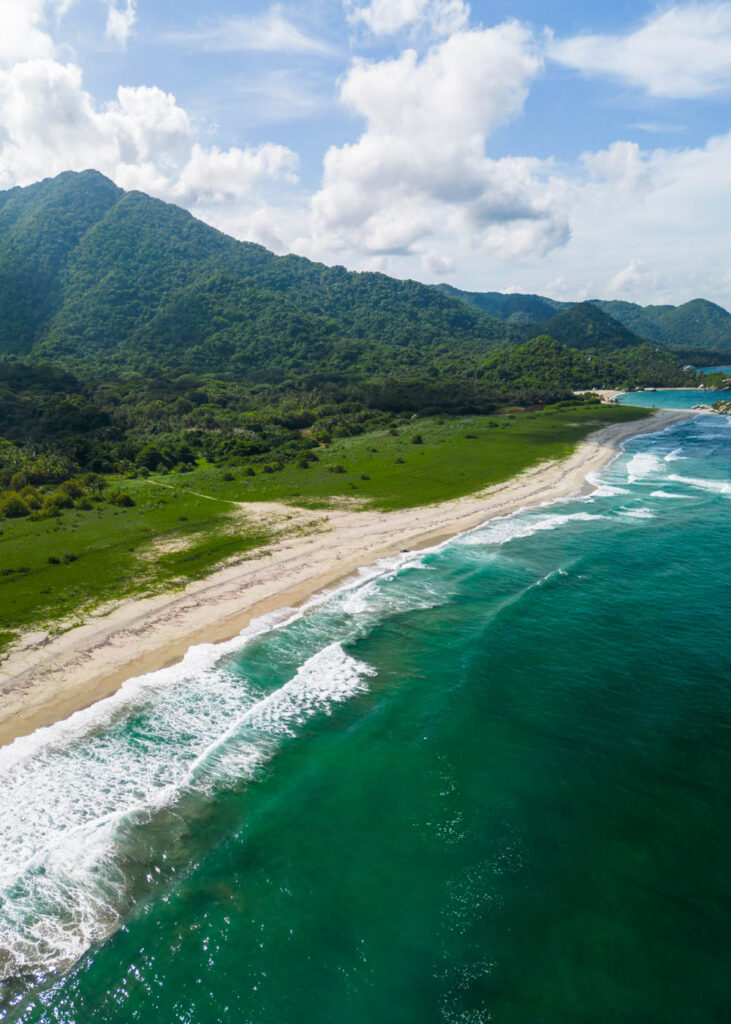 A drone view across Playa Arrecifes with Tayrona National Park's mountains in the backdrop.