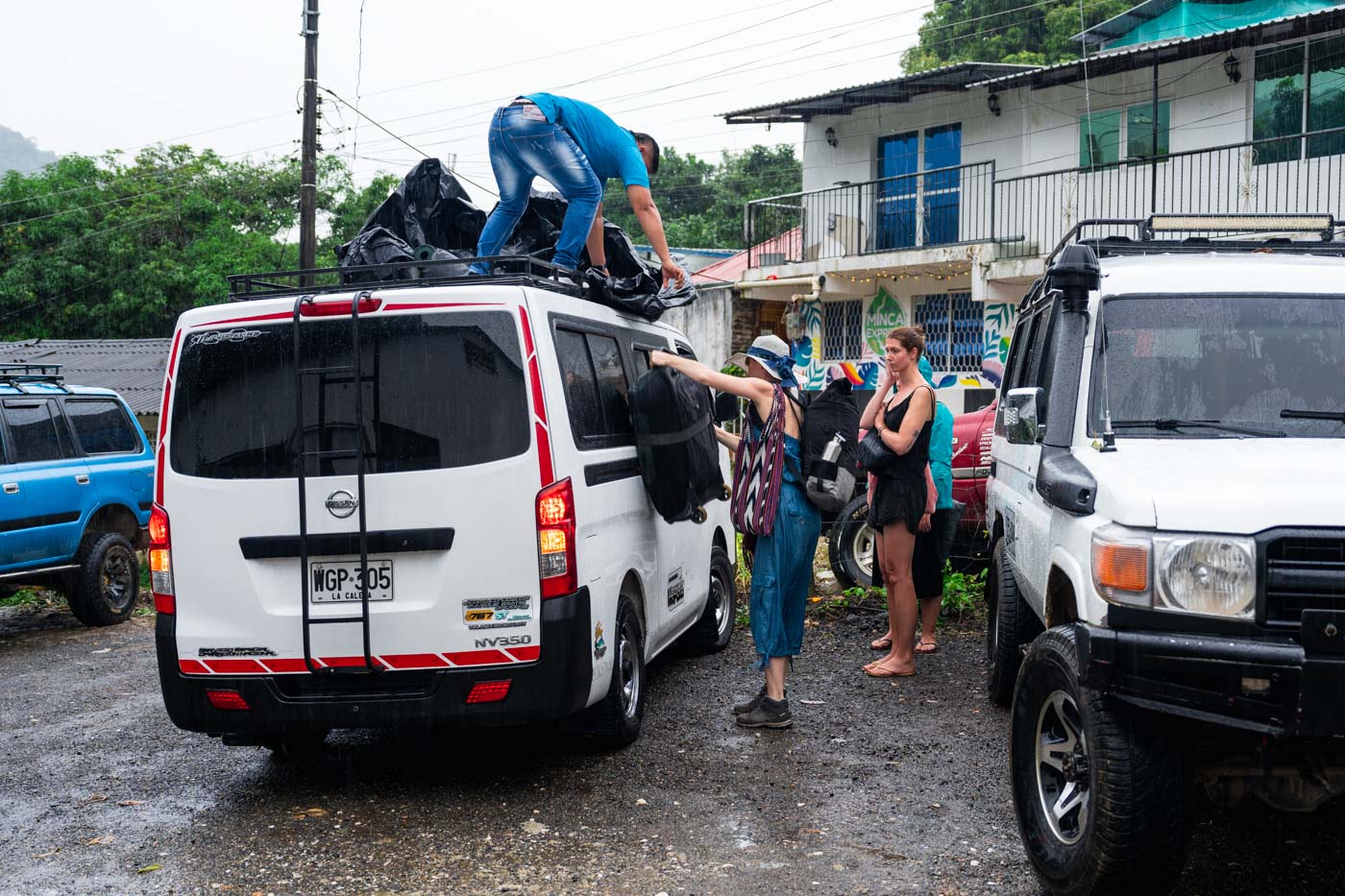 Driver handing bags in the rain to backpackers who have just arrived on the bus from Santa Marta to Minca.