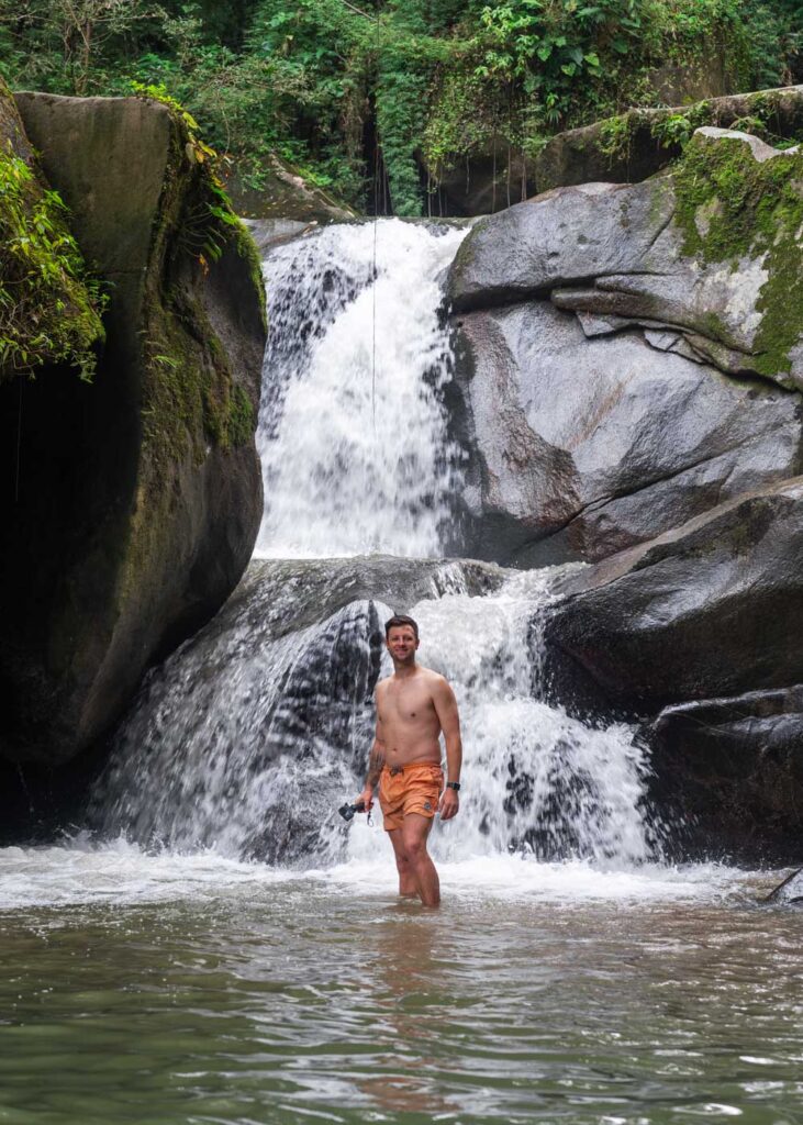 Ryan posing in front of a Cascada Oído del Mundo in orange bathing shorts.