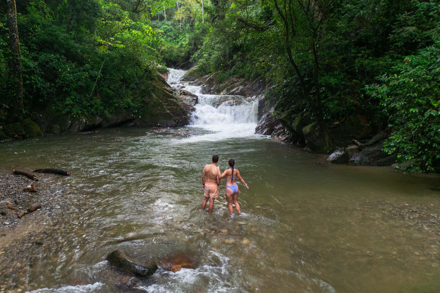 Ryan and Sara in bathing suits paddling in the river at Pozo Azul waterfall in the forest..