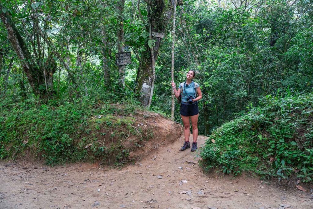 Sara standing besides the trailhead for Cascada Oído del Mundo and pointing to a sign in the forests of Minca.