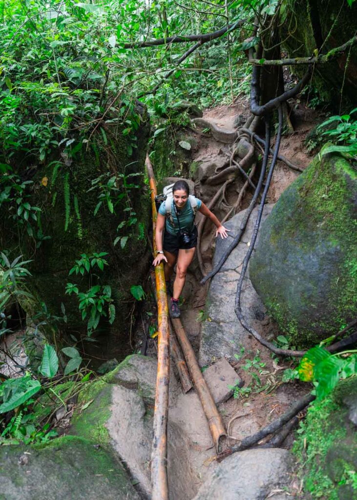 Sara crossing some boulders on a makeshift bamboo bridge and railing.