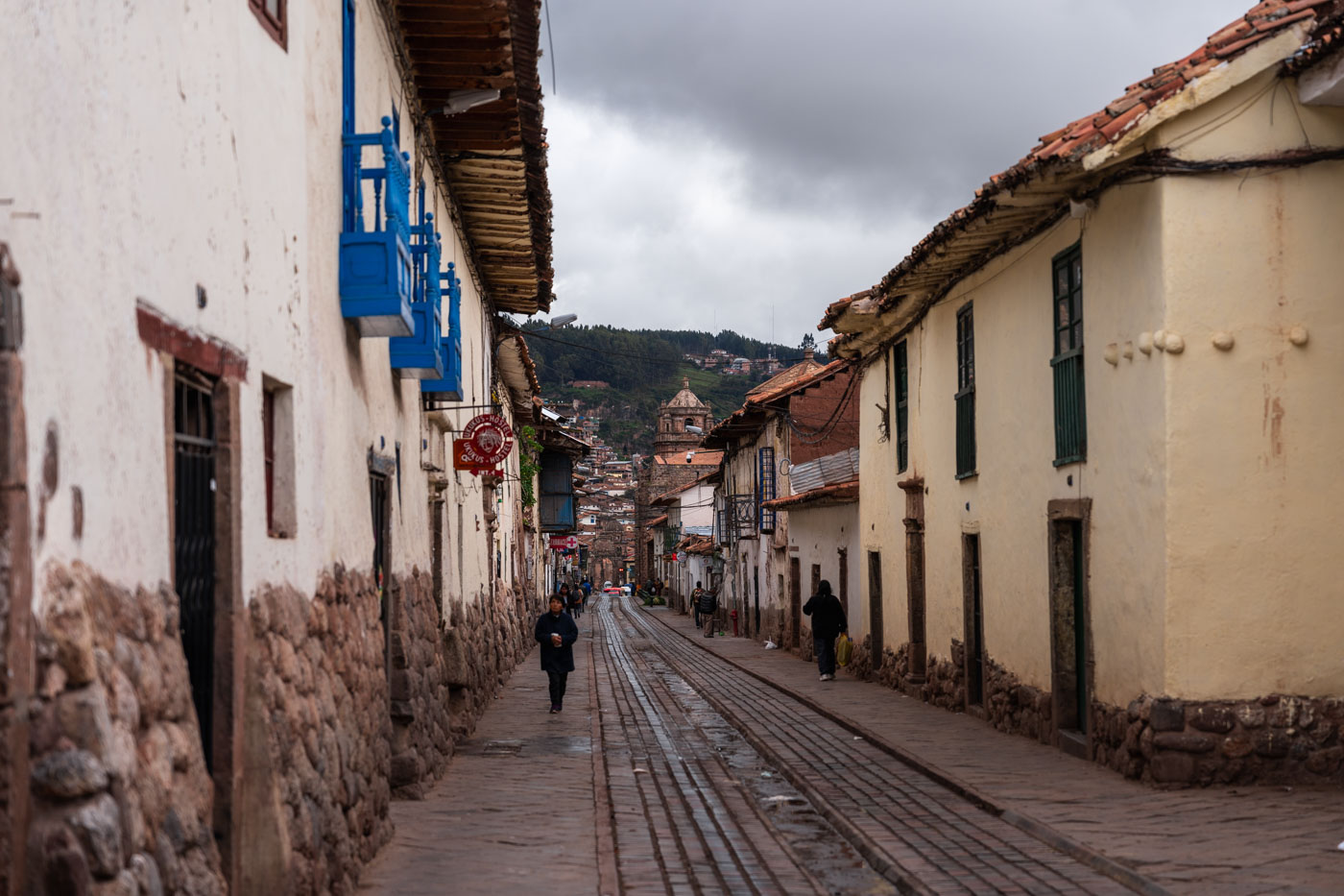 View down one of the main roads in Cusco lined with old Peruvian buildings on an overcast day.