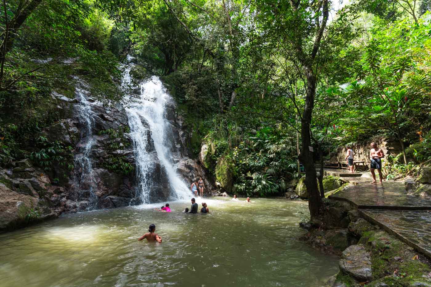 Tourists going about their day swimming in the plunge pool at the lower Marinka Waterfall in the forest.