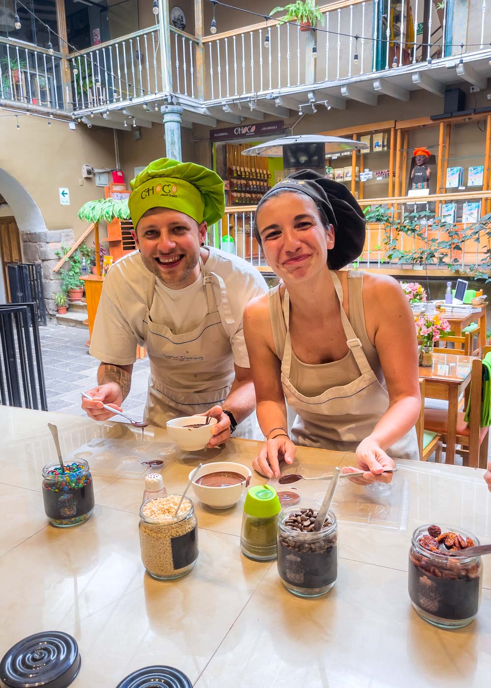 Ryan and Sara dressed in chef hats and aproms while smiling at the camera while filling molds with chocolate during a workshop at the ChocoMuseo in Cusco.