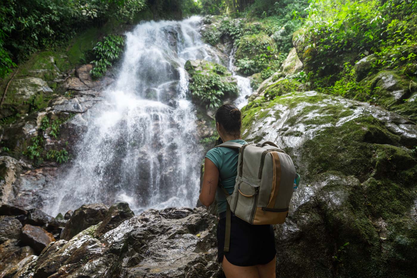 Sara in hiking gear and a backpack admiring the view of the upper Marinka Waterfall in the forest.