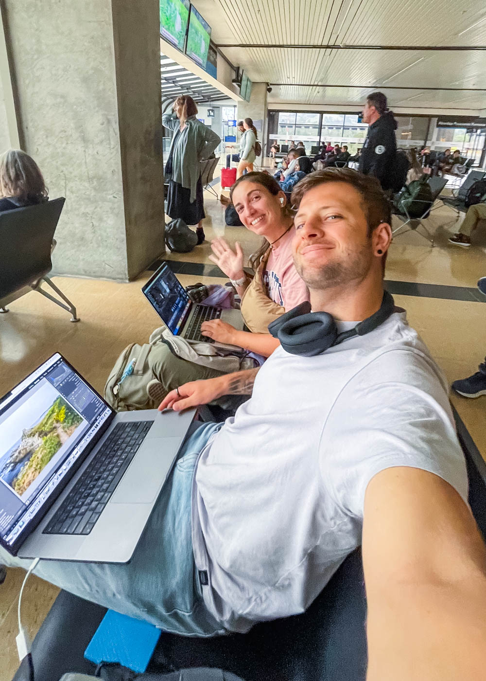 Sara and Ryan sitting in Santa Marta airport taking a selfie while working on laptops.