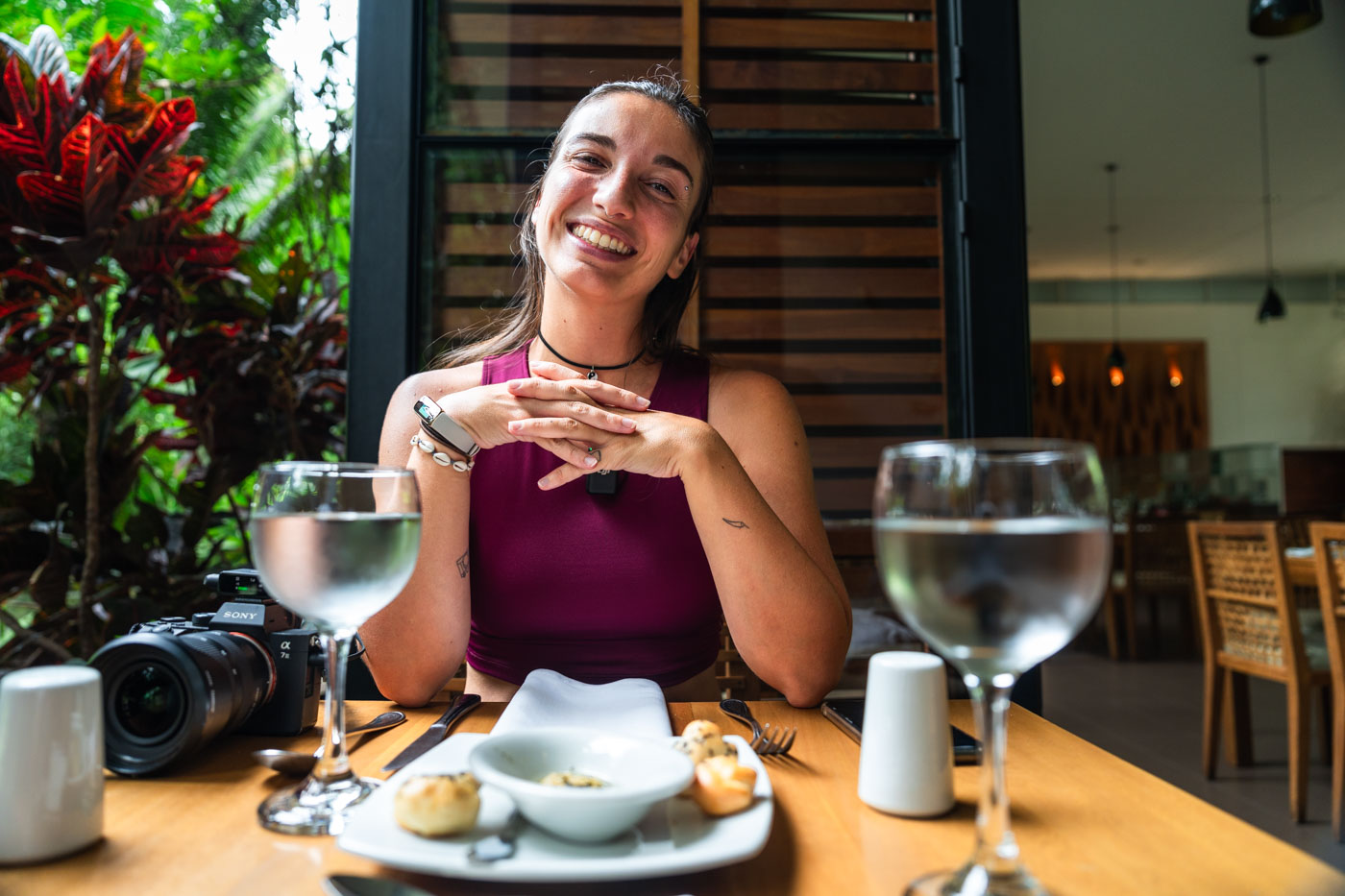 Sara sitting in a fancy restaurant with a small plate of food and wine glasses full of water at Medellin Botanical Garden.