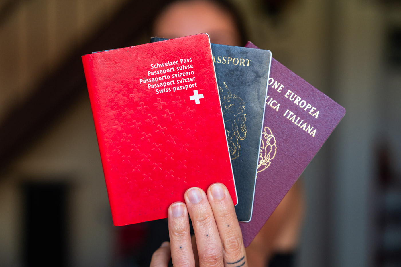 Sara holding a red Swiss, blue British and burgundy Italian passport.