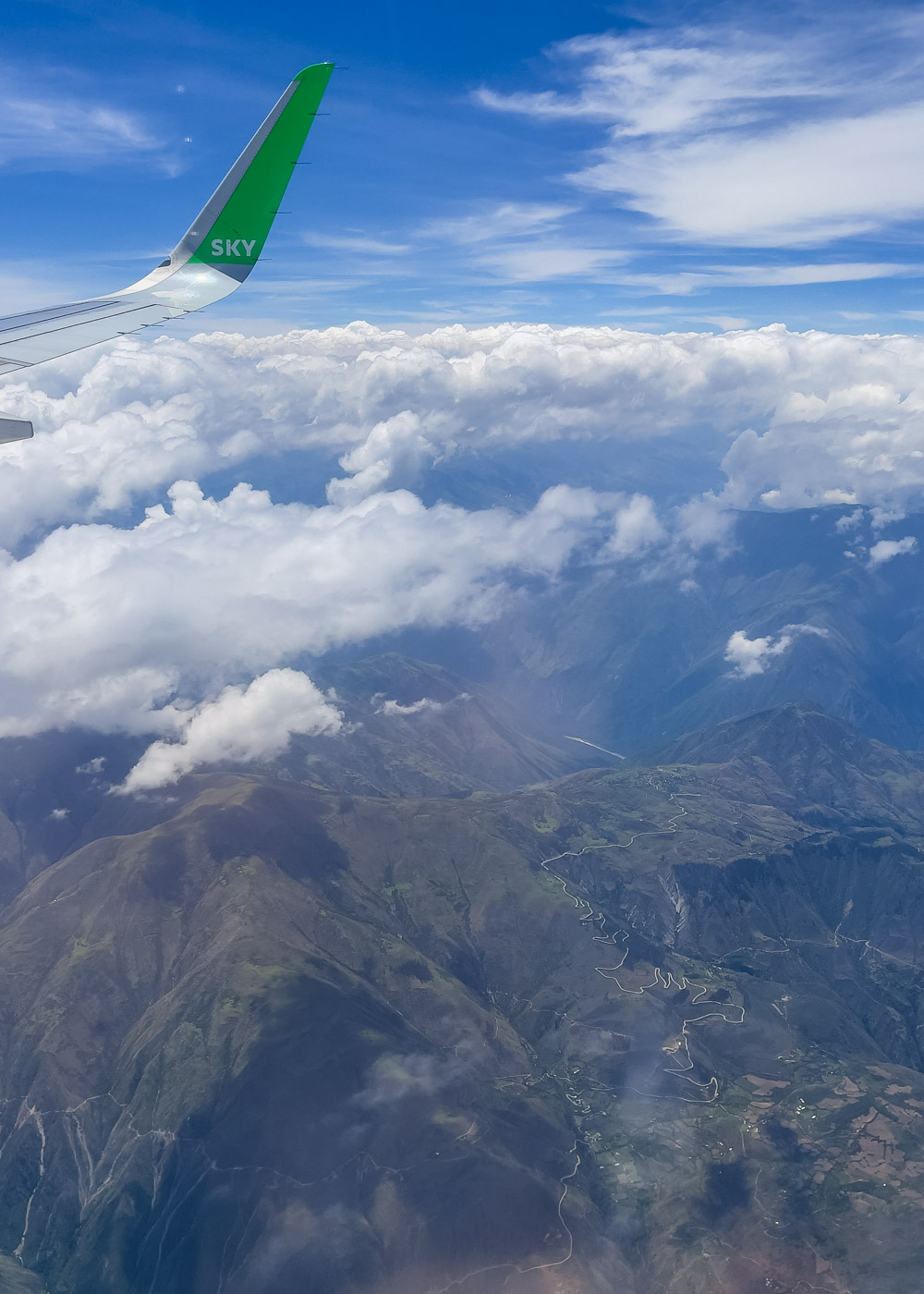 View out of an airplane window overlooking the Andes mountains and clouds above them.