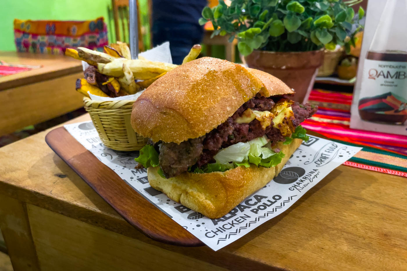A juicy looking alpaca burger with a side of fries on a wooden plate at Chakruna Native Burgers in Cusco.