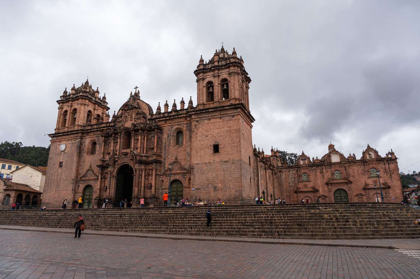 The grand architecture of the main cathedral in Cusco with tourists around it on an overcast day.