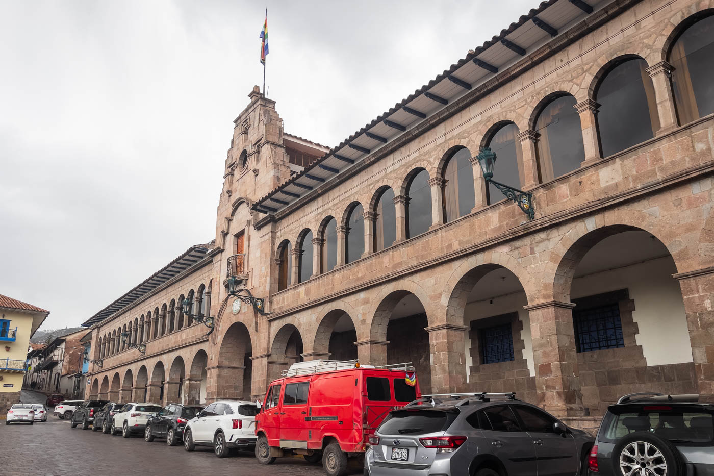 The cool looking building in Cusco that houses the Museum of Contemporary Art with cars lined up out front on an overcast day.