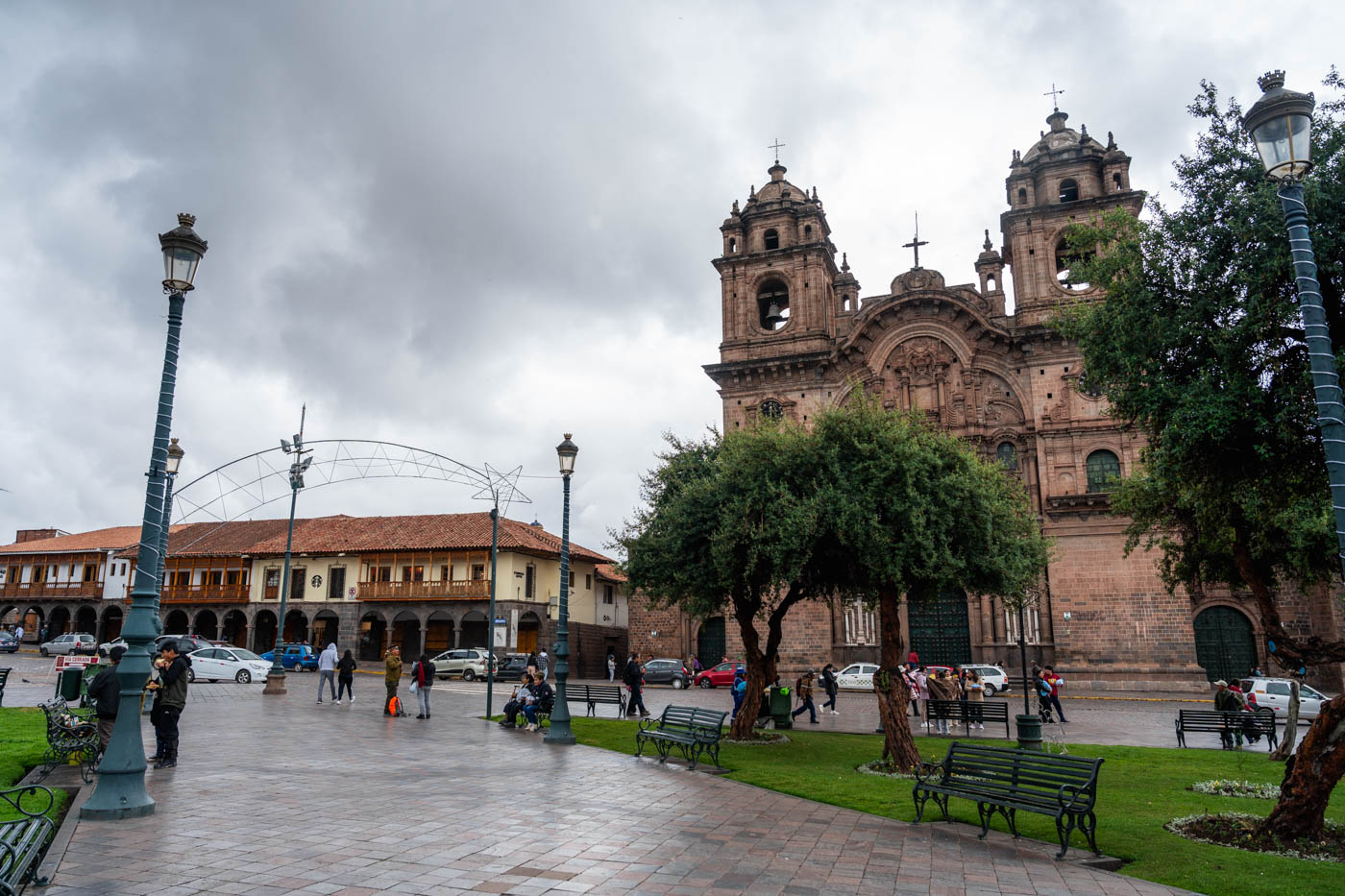 People in the park at Plaza de Armas in Cusco beside the Church of the Society of Jesus on an overcast day.