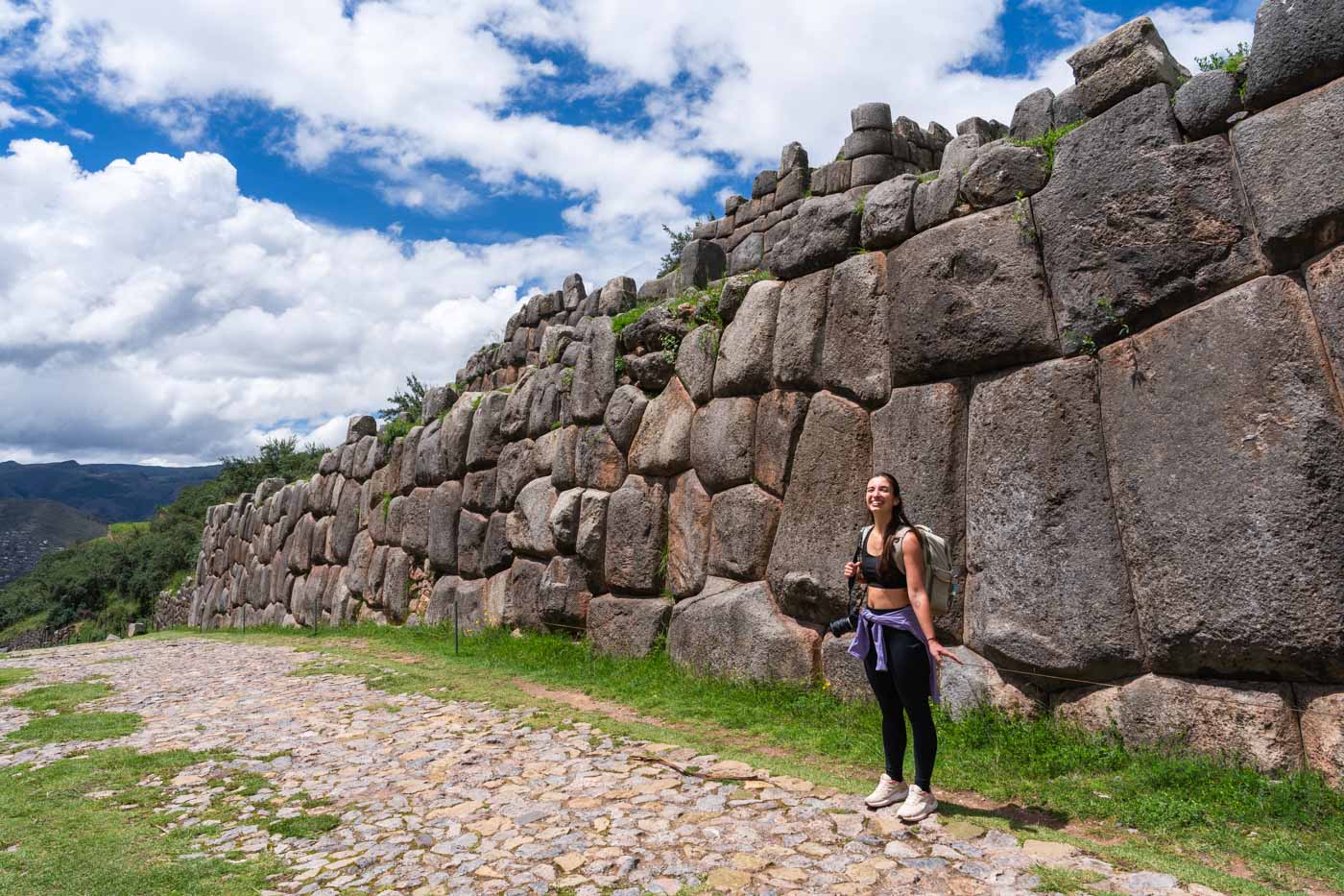 Sara wearing hiking gear and posing next to a giant Inca wall beside Saqsaywaman archeological site in Cusco.