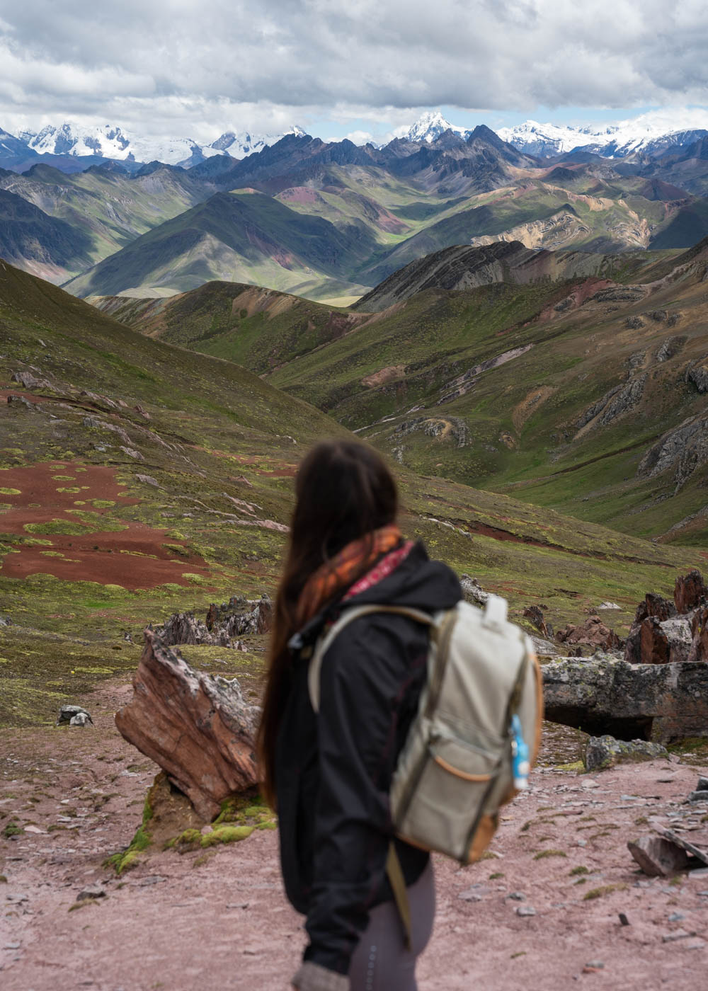 Sara in a raincoat and backpack overlooking a view of the Andes mountain range with snow-capped mountains in the distance.
