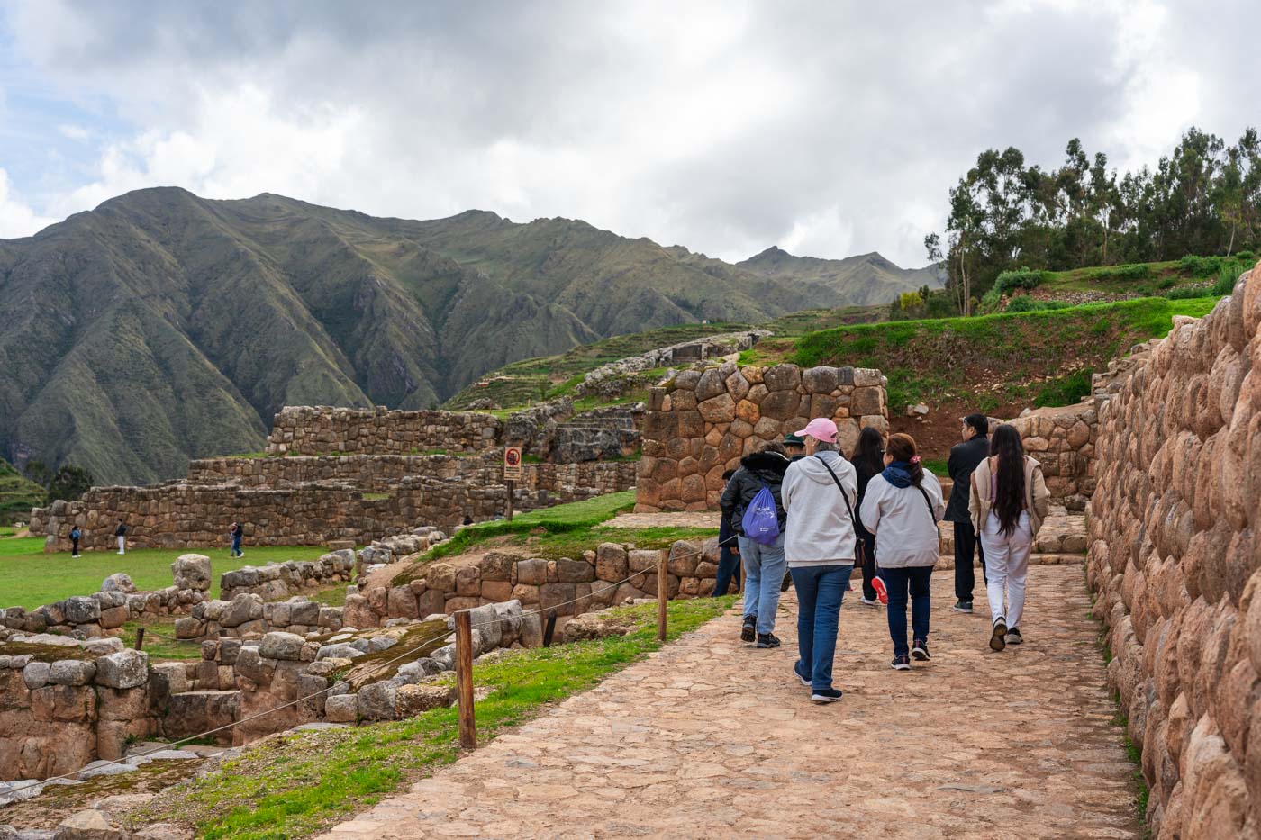 A group of tourists walking through Chinchero archeological site around the ruins of Inca walls and with a view of mountains.