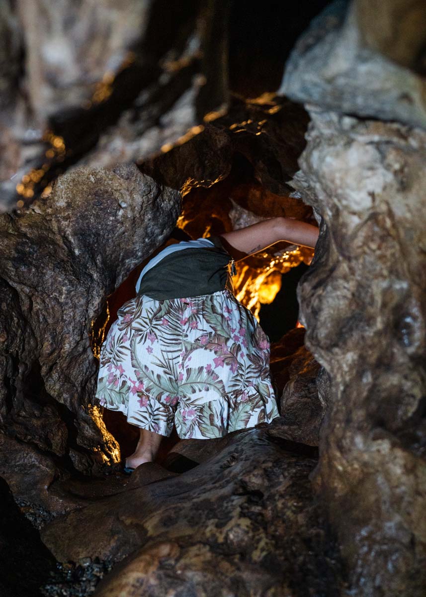 Our friend Denise climbing through a narrow gap in Chiang Dao Caves with a warm light shining at the end.