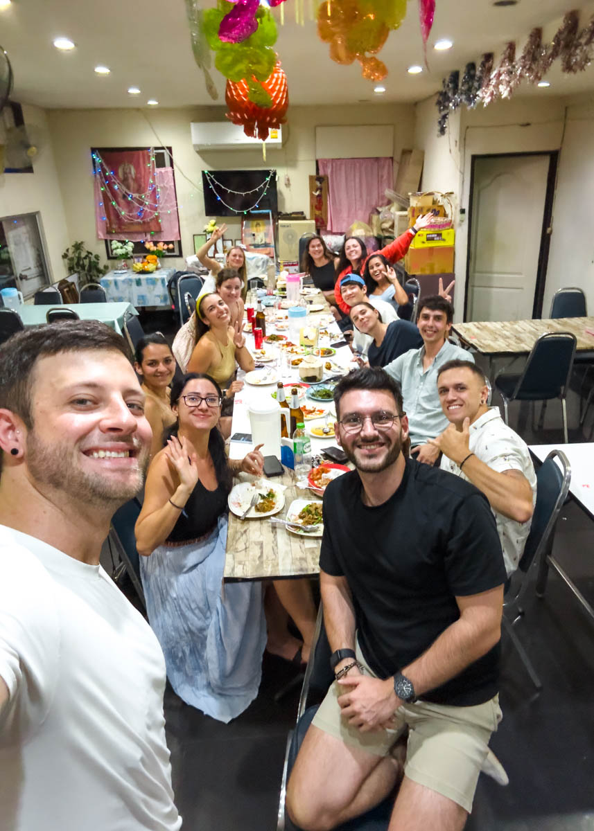 Ryan taking a selfie in front of a long table full of our digital nomad friends at a dinner in a homely looking room.