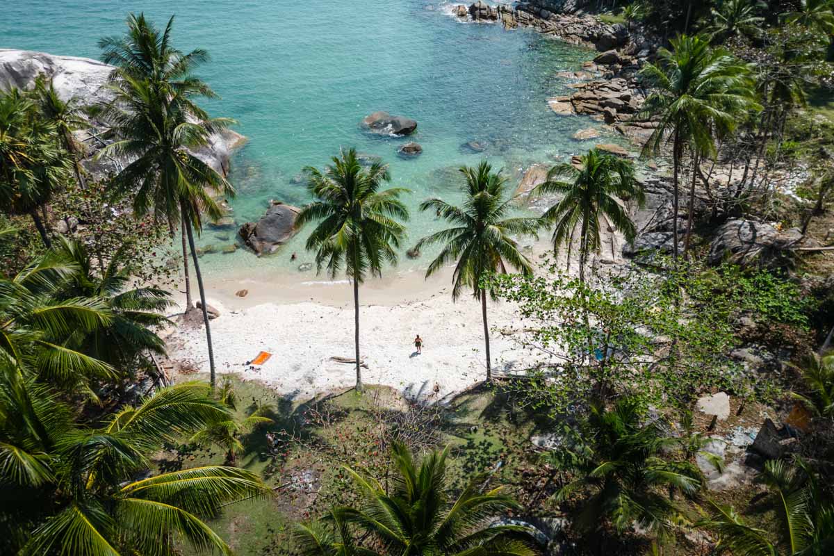 Sara standing on Than Sadet Beach, in Koh Phangan, between a row of palm trees with clear blue waters lapping against the white sand.