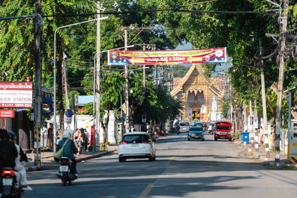 Looking down the main street that runs through the Old City while cars and scooters drive up and down. There are trees either side of the road and a golden temple in the distance.