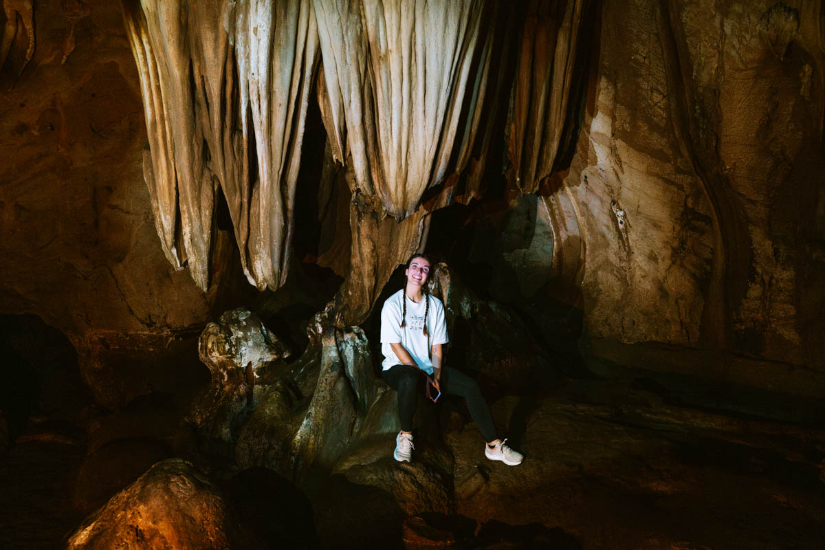 Sara sitting on a stalactite under a bunch of unique looking stalagmites inside of Chiang Dao Cave.